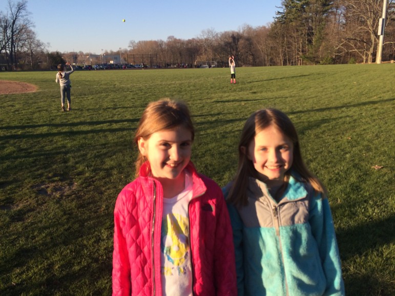 L-R: Gianna Marciano, 7, a West School first-grader, and Brooke Mellas, 7, a second-grader there, were on hand to watch their big sisters play in the 10-and-under New Canaan Softball AAA division Opening Night game at Waveny.